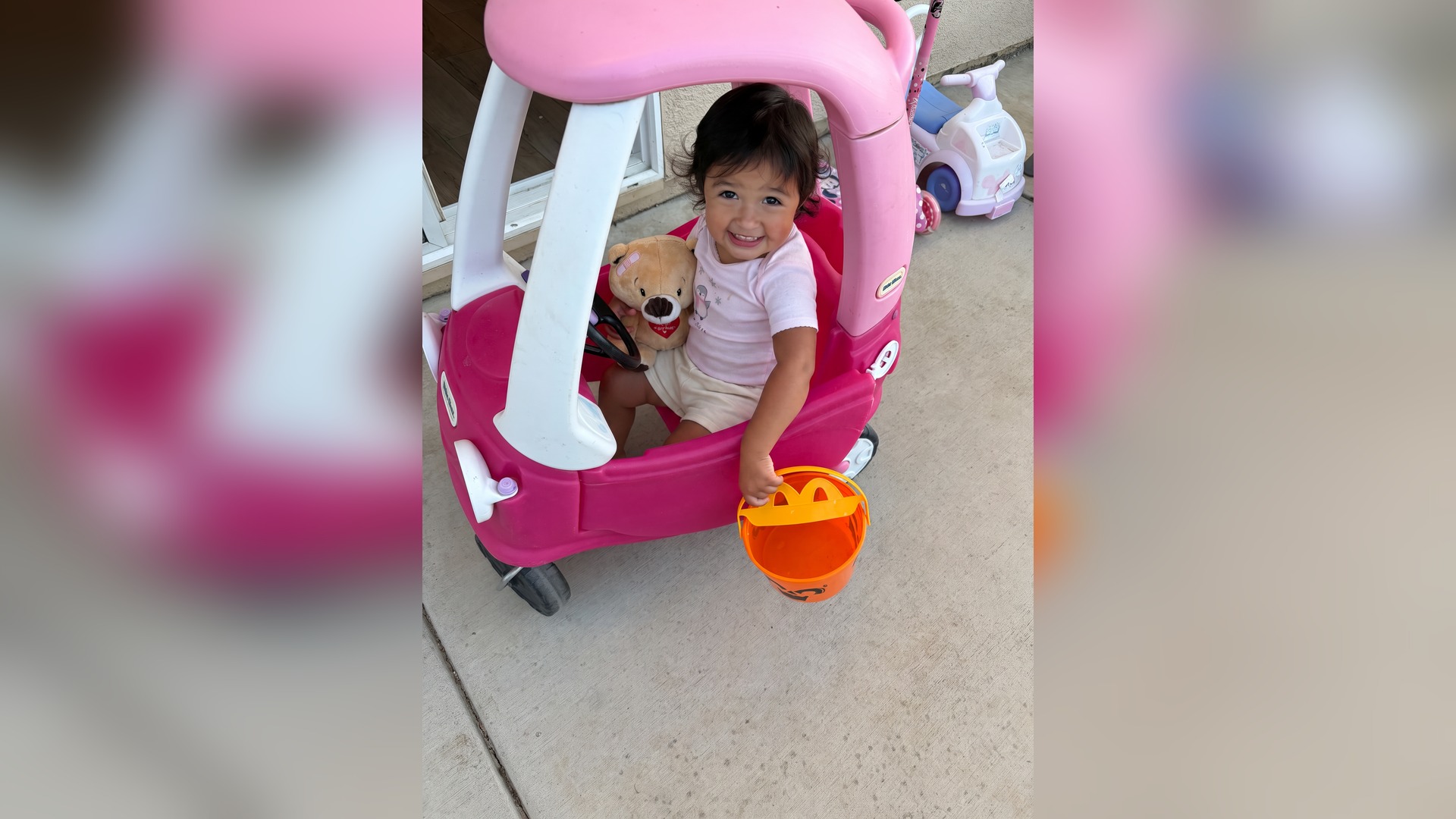 Toddler smiling in a pink toy car at Little's Childcare